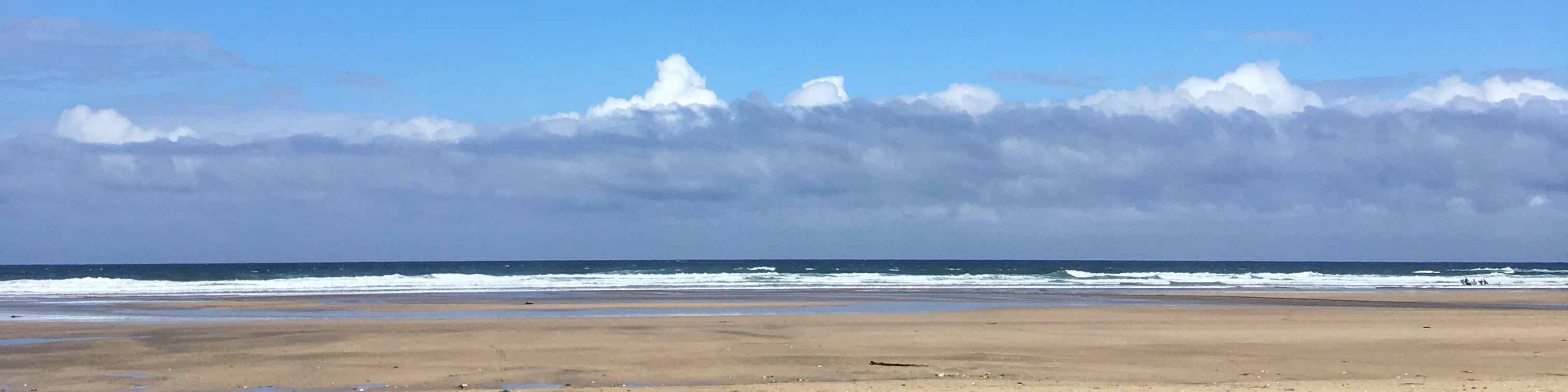 Gwithian beach on a Summer's day – golden sand, deep blue sea with white surf, blue skies and an unusual cloudscape which almost looks like snow capped mountains. Gwithian beach, Cornwall.